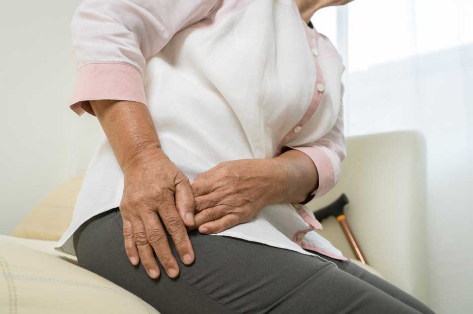 Woman with hip pain, sitting and clutching hip.